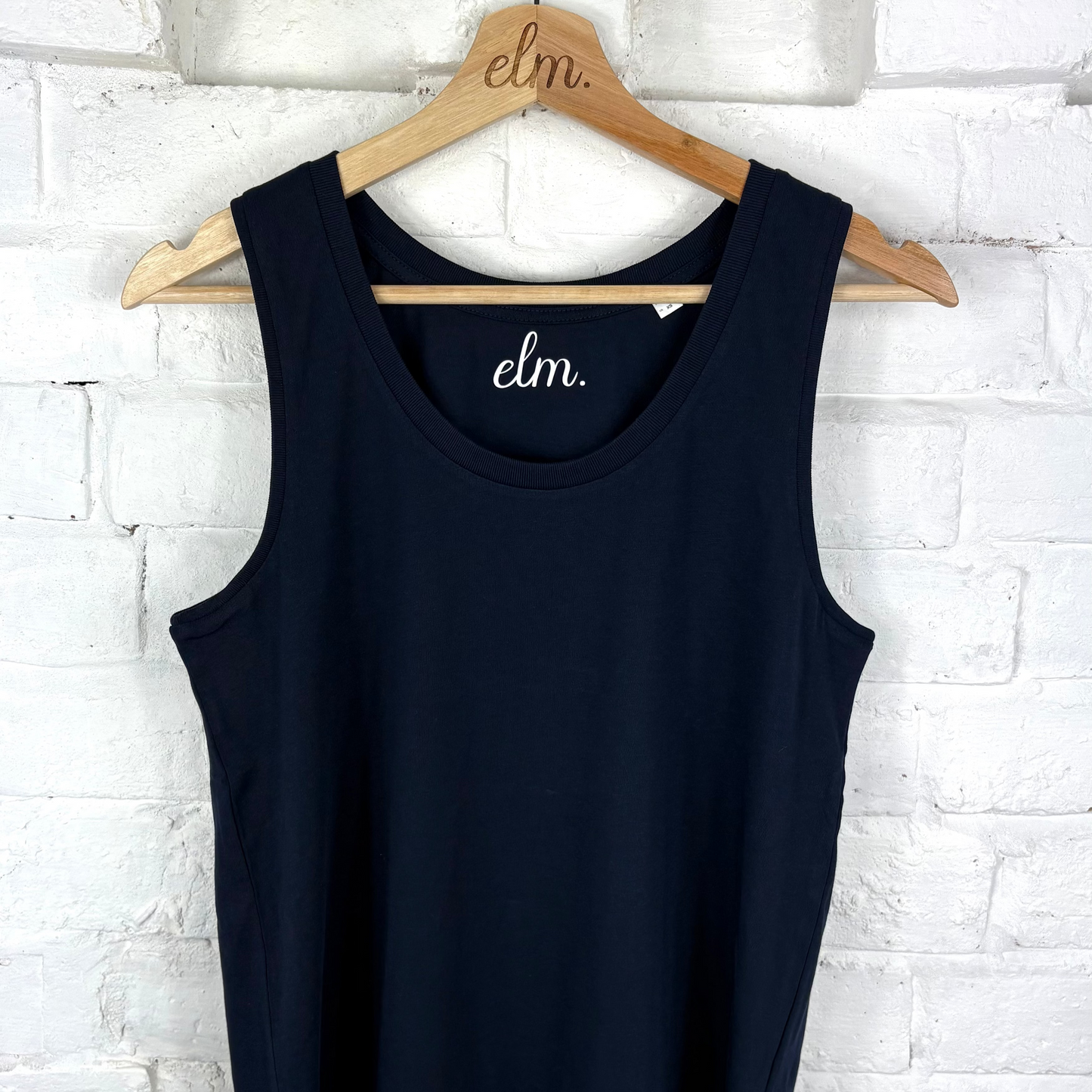 Navy tank top on a wooden hanger against a white brick wall