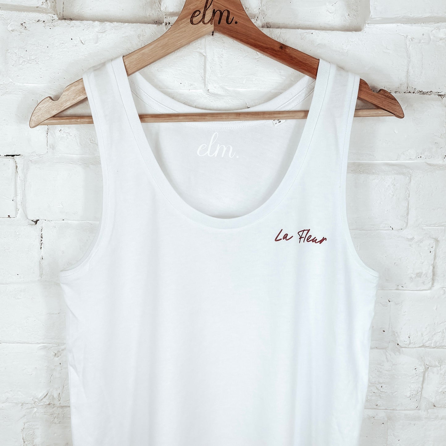White tank top on a wooden hanger against a white brick wall.